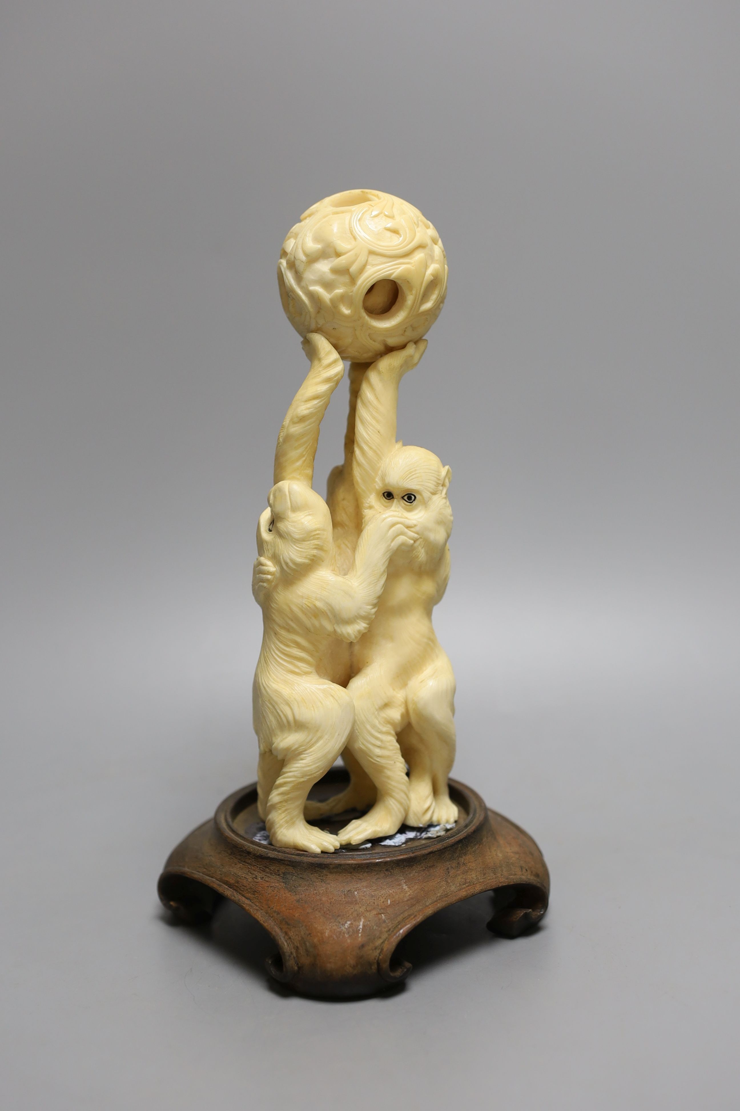 A Japanese ivory okimono of the three wise monkeys supporting a puzzle ball, early 20th century, wood stand, 20.5cm tall